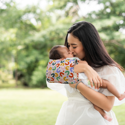 Maman embrasse son bébé avec un coussin allaitement bariolé pour soutenir confortablement dans sa promenade