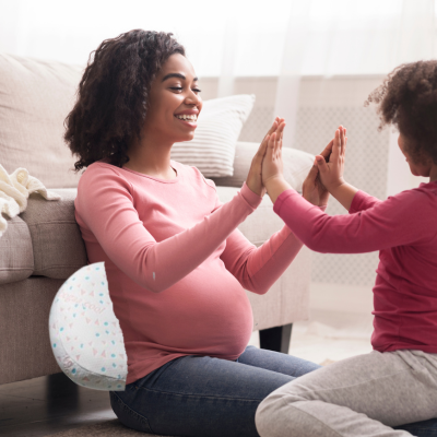 Maman qui joue avec sa fille assis sur le tapis soutenu avec son coussin grossesse.