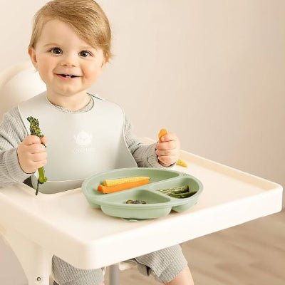 Assiette pour bebe assit devant son assiette vert